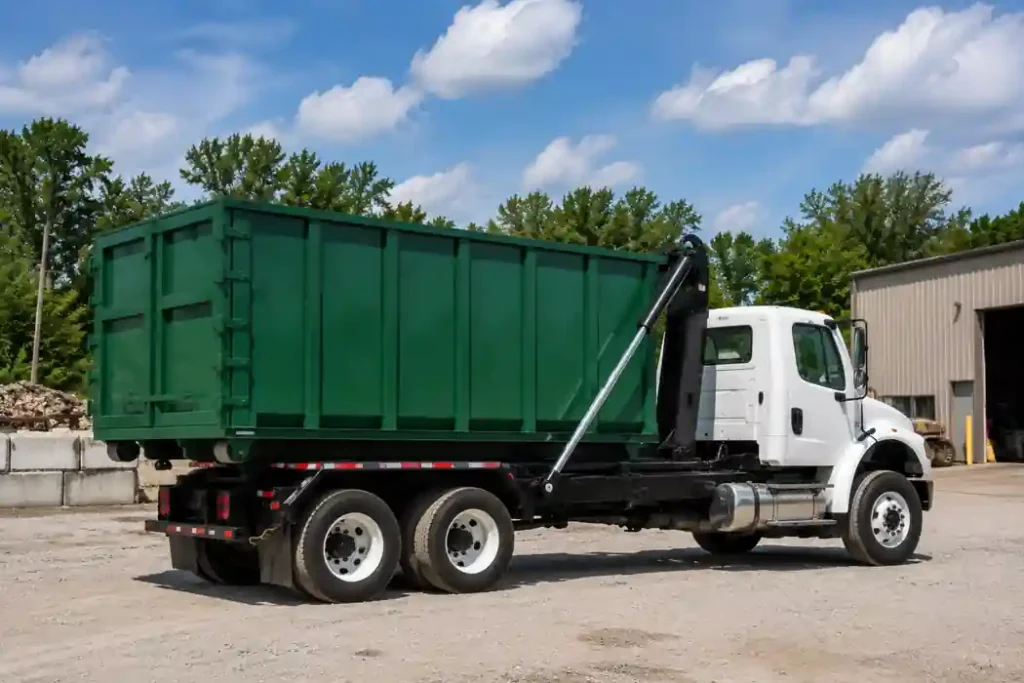Roll-Off Dumpster Rental in Asheville, NC - Fast, Local & Flat-Rate 5 White roll-off dumpster truck hauling a green 25 yard dumpster container in an industrial yard for residential and commercial dumpster rental service in Asheville NC.